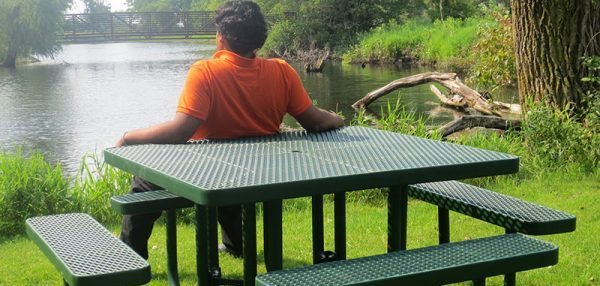 Man sitting on a commercial picnic table overlooking the river. picnic table